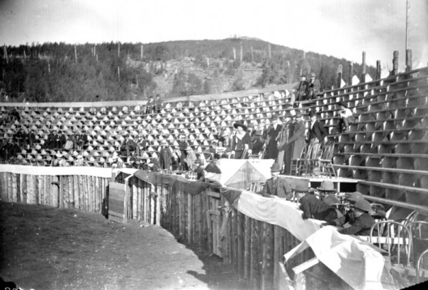 The bullfight on August 24 or 25, 1895, in the wood bullring built at the race track in Gillett, Colorado, is about to begin. Joe Wolfe, the organizer of the event and "Master of the Fiesta," wearing a Mexican sombrero, a velvet suit with silver buttons and gloves, stands in a decorated box in the stands, with four men behind him. People around look toward the bullring; there are many empty seats in the arena. The event caused a scandal because of its cruelty to animals.