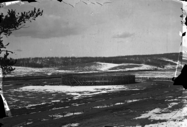 The wood bullfight ring used for the Mexican bullfight on August 24 and 25, 1895, within the racetrack at Gillett, Colorado, is empty; snow is on the ground; trees on the hills behind are leafless. Joe Wolfe was the organizer of the event which caused a scandal because of its cruelty to animals.