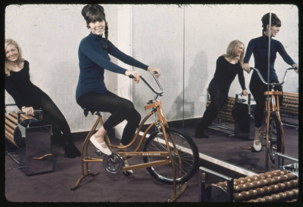 Women pose on exercise equipment in front of a wall mirror at the cub house in the Green Mountain Townhomes complex in Lakewood, Colorado. One woman sits on an exercise bike, another sits on the edge of a roller massager.