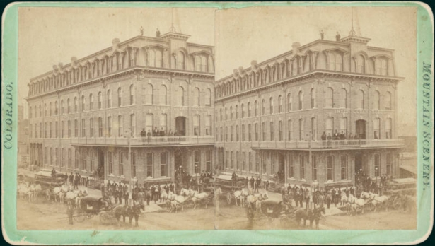 View of the Inter Ocean Hotel, built by Barney L. Ford on the corner of 16th (Sixteenth) and Blake Streets in Denver, Colorado; shows a four story brick hotel with a mansard roof, pedimented dormers and keystones above arched windows. Men stand near a finial on the roof.  People stand on a balcony on the front of the building. Men pose near a horse-drawn carriage and horse-drawn omnibus in the street.