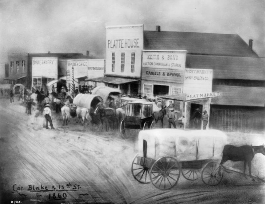 Painting of the corner of Blake and 15th (Fifteenth) streets, in Denver, Colorado. Shows covered wagons, people, and false front businesses. Signs read: "Meat Market, Shaw-Bailey & Co.," "Keith & Bond, Auction, Commission & Storage," "Daniels & Brown," "Platte House," "Ford's Barbershop," "Heatley Chase," "[?] Beer," and "Empire Bakery."
