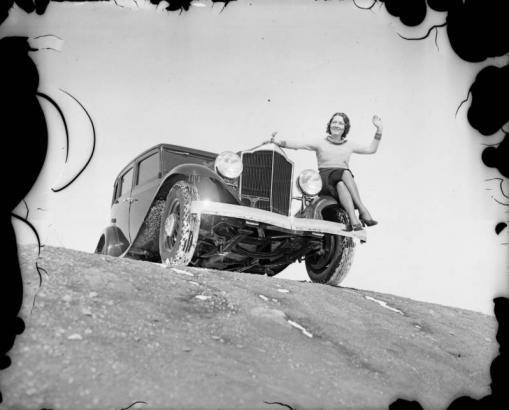 A woman poses on the fender of an automobile probably in Colorado.