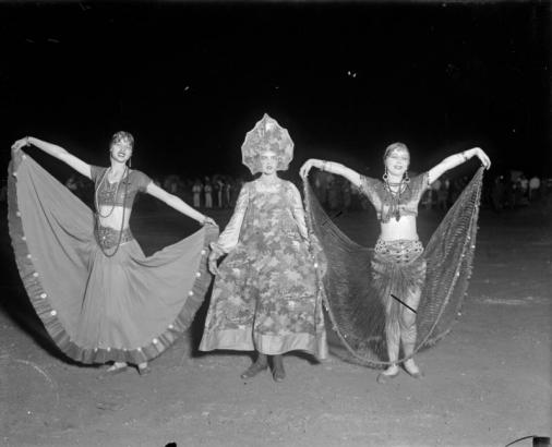 Women pose in costumes that include: lace, brocade, beads, wide dresses, robes, and a scalloped headdress.