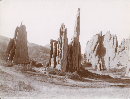View of Cathedral Spires, a sandstone rock formation at Garden of the Gods near Colorado Springs (El Paso County), Colorado. Shows a dirt road and brush.