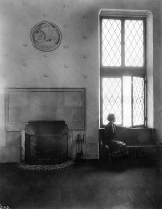 Interior view of the Park Hill Branch of the Denver Public Library in Denver, Colorado; decor includes a fireplace, shell motifs, and a ship medallion carved by Robert Garrison. A woman sits by leaded glass windows.