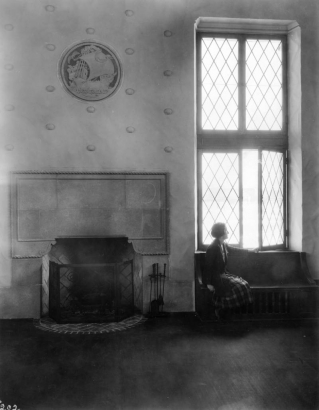 Interior view of the Park Hill Branch of the Denver Public Library in Denver, Colorado; decor includes a fireplace, shell motifs, and a ship medallion carved by Robert Garrison. A woman sits by leaded glass windows.