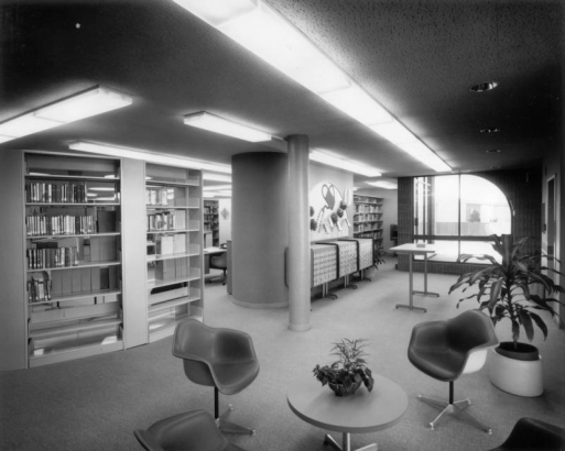 Interior view of the Bear Valley Branch of the Denver Public Library in the Harvey Park South neighborhood of Denver, Colorado; decor includes molded plastic chairs, curved window frames, a dracena plant, and card catalog cabinets.