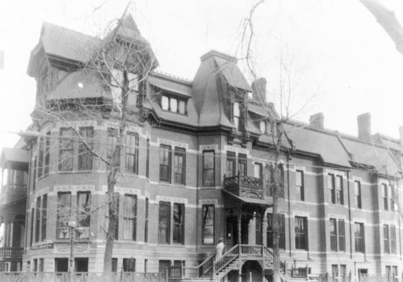 View of Denver Public Library at La Veta Place, at Bannock and Colfax Streets in Denver, Colorado; features bay windows, stone lintels, gables, and ridgecresting. A woman is on the steps; sign reads: "Public Library" and "La Veta Place."