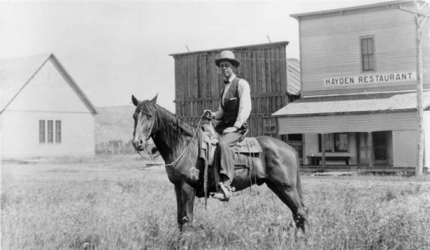 Farrington Reed Carpenter, lawyer, rancher, and the first director of grazing for the Department of the Interior, poses on horseback in Hayden (Routt County), Colorado. A false front building in the distance has a sign that reads: "Hayden Restaurant."