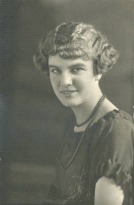 Elizabeth Kieffer poses for her South High School senior portrait in Denver, Colorado. Adler's hair is styled in a wavy bob with bangs and she wears a scooped neck blouse with a beaded flower, and probably a bead necklace.