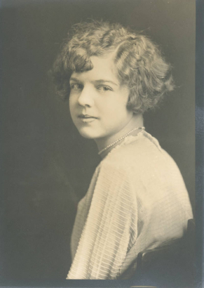 Anna May Bornhauser poses for her South High School junior portrait in Denver, Colorado. Bornhauser's hair is styled in a wavy bob and she wears a woven long sleeved blouse and a pearl necklace.