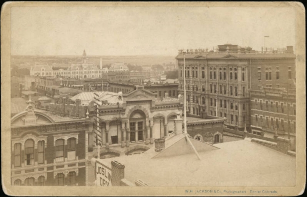 Rooftop view of commercial buildings in the Union Station neighborhood of Denver, Colorado. Multi-story brick and stone buildings on 16th (Sixteenth) Street include the Hotel Brunswick (Clarke Building), the corner Tabor Block and the "New York Hotel." The Riche Building and Joslin's Dry Goods building are on the 300 block of Lawrence Street. Union Station is in the distance.