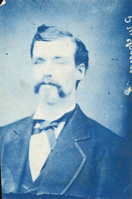 Studio portrait of Patrick McCann, an employee in a reduction works in Georgetown (Clear Creek County), Colorado. He wears a coat with bound, wide lapels, a vest, a shirt with an upright collar and a bow tie. His dark hair is parted on the side and combed into a cowlick. He has a long mustache.