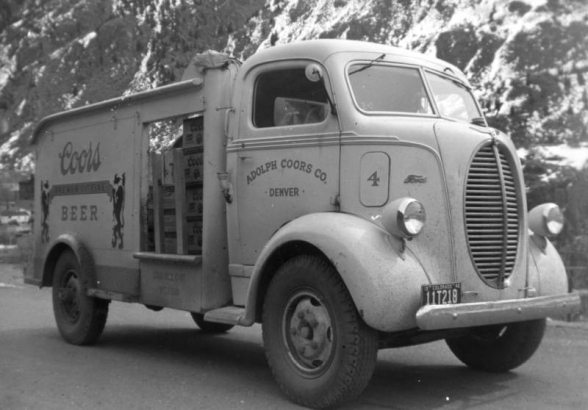 A Ford Coors delivery truck parks on a Colorado street with cases  of beer showing through side door. Lettering on truck reads: "Adolph Coors Co. Denver" and "Coors Brewer of Fine Beer."