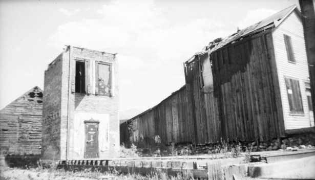 View of a disassembled sidewalk leading up to the ruins of the old court house, Breckenridge, Colorado; features a single leaf door with  decorative moulding and a wood beam running from the ground to the top of the building; other dilapidated buildings are near the court house.