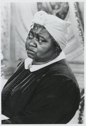 Actress Hattie McDaniel [Graduate of Denver's East High School] poses in her role as "Mammy" from the motion picture "Gone With The Wind." She wears a dark blouse, cameo, and scarf tied around her head.