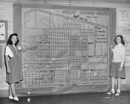Girls pose by a wall-sized map of the Park Hill District at Smiley Junior High School, in Denver, Colorado. Lettering at the top reads: "Smiley Housing Survey, Park Hill District."