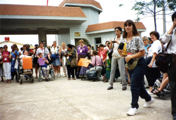 Laura Hershey, Robin Stephens and a large group of women protesting the lack of access to United Nations Fourth World Conference on Women in Beijing, China in August 1995. Robin Stephens is holding up a sign that says ""Build Ramps Not Bombs."" In foreground (right) is friend Laurie Gery. Photographer unknown.