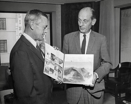 Melvin J. Roberts, right, president of the Denver Clearing House Assn., holds up a copy of the Denver Olympic Committee's presentation book, used to win the United States competition. Roberts was presented with [the] book by Thomas Hildt, Jr., vice-president of finance for the Denver Olympic Committee, after receiving a check for $10,000 as This year's contribution from the assn. The money will be used in the DOC's 1968 budget for promotional expenses to win international designation for 1976 Winter games.