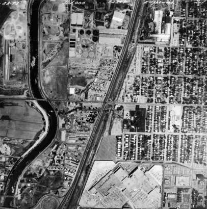 In an aerial view of Englewood, Colorado, Cinderella City Shopping Center, the South Platte River, Santa Fe Drive (U-85), residential neighborhoods, and industrial buildings, including a factory, are visible.