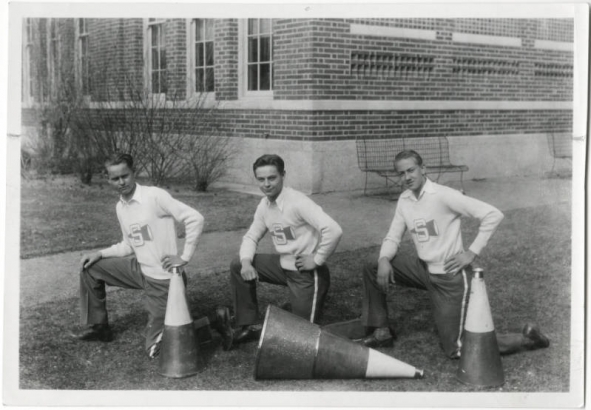 Three male cheerleaders from South High School in Denver, Colorado pose on one knee with their megaphone for a team picture. Taken at 1700 East Louisiana Avenue, Denver, Colorado, 80210.