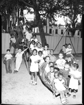 Thirty-Five students of the George Washington Carver Day Nursery school pose on the playground side at the school's 2357 Clarkson playground. One child hangs upside-down from underneath the slide.