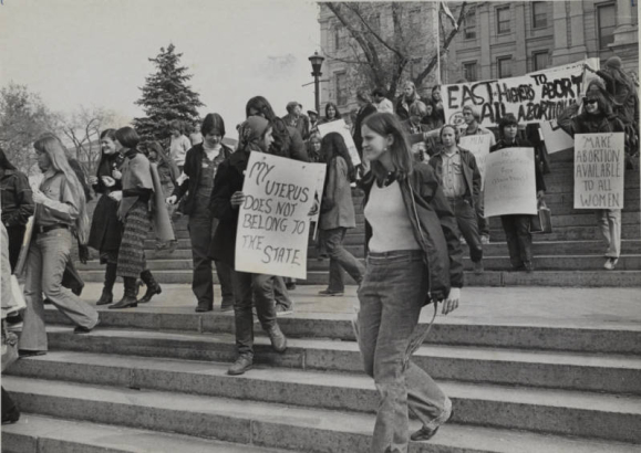 An estimated 200 persons, mostly young women, marched in support of the repeal of all abortion laws. The march was sponsored by Coloradans to Abolish All Abortion Laws and acts as a prelude to the others that were planned for San Francisco and Washington, D.C. on November 20, 1971. They holds signs that read [left to right]: "My uterus does not belong to the state," "no prosecution for abortion," and "make abortion avaliable to all women." In the back a sign reads: "East Highers to abort all abortions."