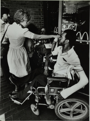 A woman climbs over David Sheckles [right] and Bob Conrad [left] in order to get into the McDonald's restauraunt on Colfax Avenue and Pennsylvania Street. The protestors are blocking entrances demanding wheelchair access so that the experience of indoor dining can be available to all patrons (universal design) and accessible to people with disabilities (barrier-free design). 