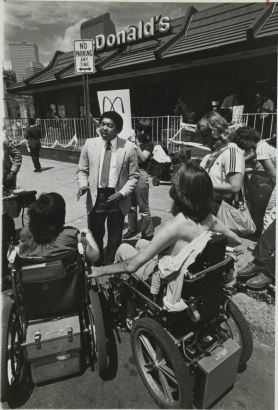 McDonald's official Dennis Morris talks with spokespersons for a group of protestors that use wheelchairs. The protestors are blocking entrances to the McDonald's located on Colfax Avenue and Pennsylvania Street demanding wheelchair access so that the experience of indoor dining can be available to all patrons (universal design) and accessible to people with disabilities (barrier-free design). 