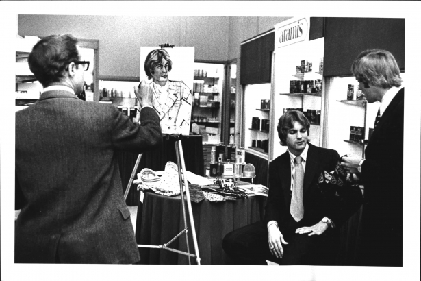 A man in a suit and tie sits while another main sketches his portrait