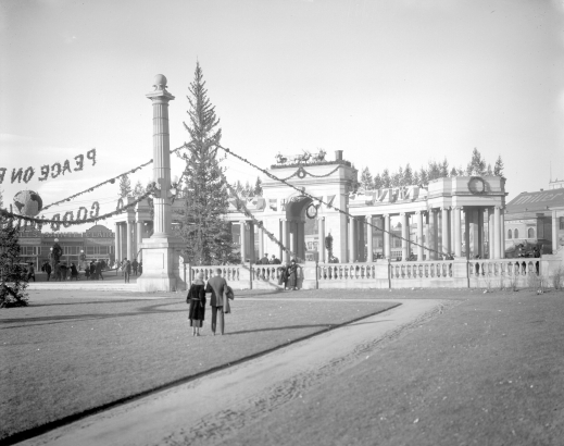 A couple stands on the grassy plaza in front of the Greek Amphitheater, an arched colonnade of Ionic columns, in Civic Center in Denver, Colorado. The structures are decorated with garland, wreaths, and a replica of Santa Claus and eight reindeer.