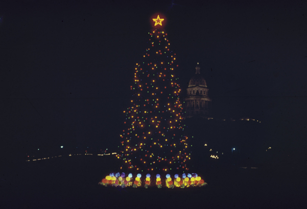 Nighttime view of a Christmas tree decorated with lights at Civic Center Park in Denver, Colorado. The Colorado State Capitol building is in the distance.