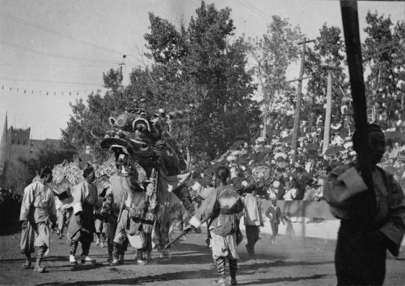 Men (Chinese - American) dressed in traditional chinese clothing walk along side a chinese dragon during the Festival of Mountain and Plain parade in Denver, Colorado. Spectators watch from the grandstands.