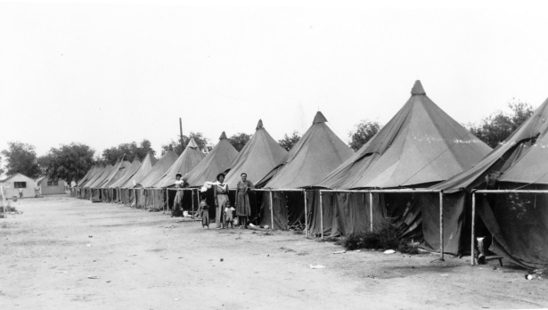 Hispanic women and children stand near a group of tents in Fort Lupton (Weld County), Colorado. The women wear dresses.
