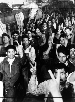 Mexican migrant workers sit in a bus in Colorado. They hold their hands up in a sign for "victory."