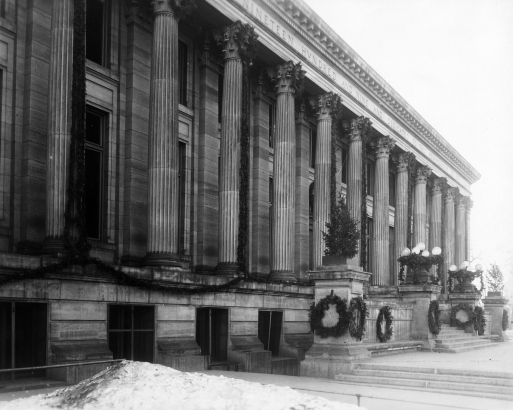 View of the Denver Public Library at Colfax Avenue and Bannock Street in the Civic Center neighborhood of Denver, Colorado. The Greek Revival style building has Corinthian columns and is decorated with greenery for Christmas.