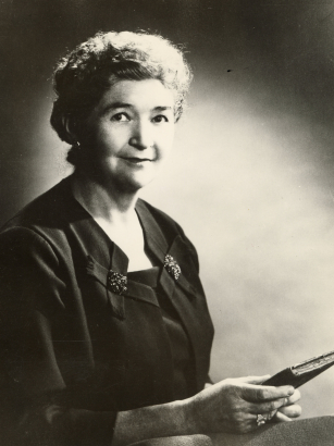 Portrait of Agnes Wright Spring, posing in a black blouse and holding a book.