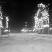 Night view of Curtis Street in Denver, Colorado; shows snow and movie theaters. Electric signs read: "Marquette," "Iris Theater," "Isis," and "The Nanking Chop Suey, Pool."