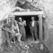 Men pose by the Lady Belle mine entrance south of Eagle, Eagle County, Colorado; one man shovels ore into a canvas bag.