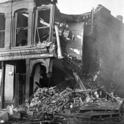 Destroyed corner section of Tutt and Penrose Building caused by second fire on April 29, 1896, Cripple Creek, Colorado; two-story commercial stone and brick building burned with corner demolished to rubble; remaining structure includes cornice with parapet and decorative crown, arched windows, wooden floor and beams, circular light hanging from coursework.