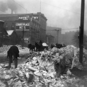 Men shovel and haul soot covered snow and ice from a downtown street, Denver, Colorado. Lettering painted on a brick building reads: Court Place Hotel.