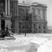 View along a snow shoveled walkway next to the Indian and buffalo bronze sculpture, "Closing era", on the back side of the State Capitol Building, Denver, Colorado. A small sign is barely visible above the deep snow, it reads:"Keep off the grass".