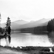A man sits in a touring automobile on Cody Road, along Sylvan Lake, Yellowstone National Park, Wyoming; Top Notch Peak shows in distance.