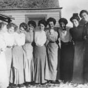Group view of nine females, Cripple Creek, Colorado; women posed standing with arms around each other's shoulders or waists; partial view of wooden frame residence in the background; women identified on back of photoprint as: June Kennedy, Donna McDonald, Mary Crane, Ruth Welty, Gertrude Joyce, Amelia Herron, Fay McDonald, Alda Stevens, Tira (or Tura?) Bentley.