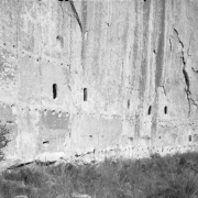 Windows and bird nest holes show in the soft volcanic rock of a verticle tuff cliffside with natural caves, Frijoles Canyon, Bandelier National Monument, New Mexico.