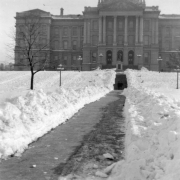 Two men walk on the sidewalk in front of the State Capitol Building cleared of deep snow from the December 1913 storm, Denver, Colorado.