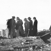 Group of men inspect remaining bank safe amidst debris and rubble  from second fire on April 29, 1896, Cripple Creek, Colorado; one man wears  sherriff badge on overcoat.