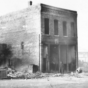 Fire-gutted exterior view of two-story, flat roof, single story brick commercial building, Bennett Avenue, caused by second fire of April 29, 1896, Cripple Creek, Colorado; decorative cornice.
