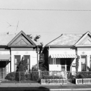 View of 2357 and 2361 Curtis Street in the Five Points neighborhood of Denver, Colorado.  Shows a pair of matching Queen Anne-style single family residences.  The one-story brick houses have a pedimented front gable window bay, scroll-sawn bargeboards, molded plaster rosettes, and decorative carved lintels.