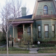 View of the Scobey House (c. 1882) at 2826 Curtis Street in the Five Points neighborhood of Denver, Colorado. This one-and-one-half-story brick residence shows characteristics of Second Empire and Late Victorian styles. Features include wood trim, iron cresting, and a mansard-roof extension. William Allen West, the owner, is standing next to the porch decorated with scroll-sawn brackets.